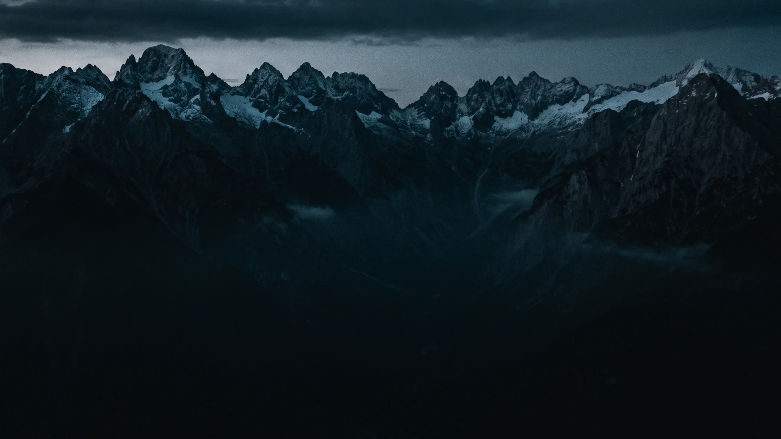 Aerial view of a jagged, snow-dusted mountain ridge at dusk above a dark valley.