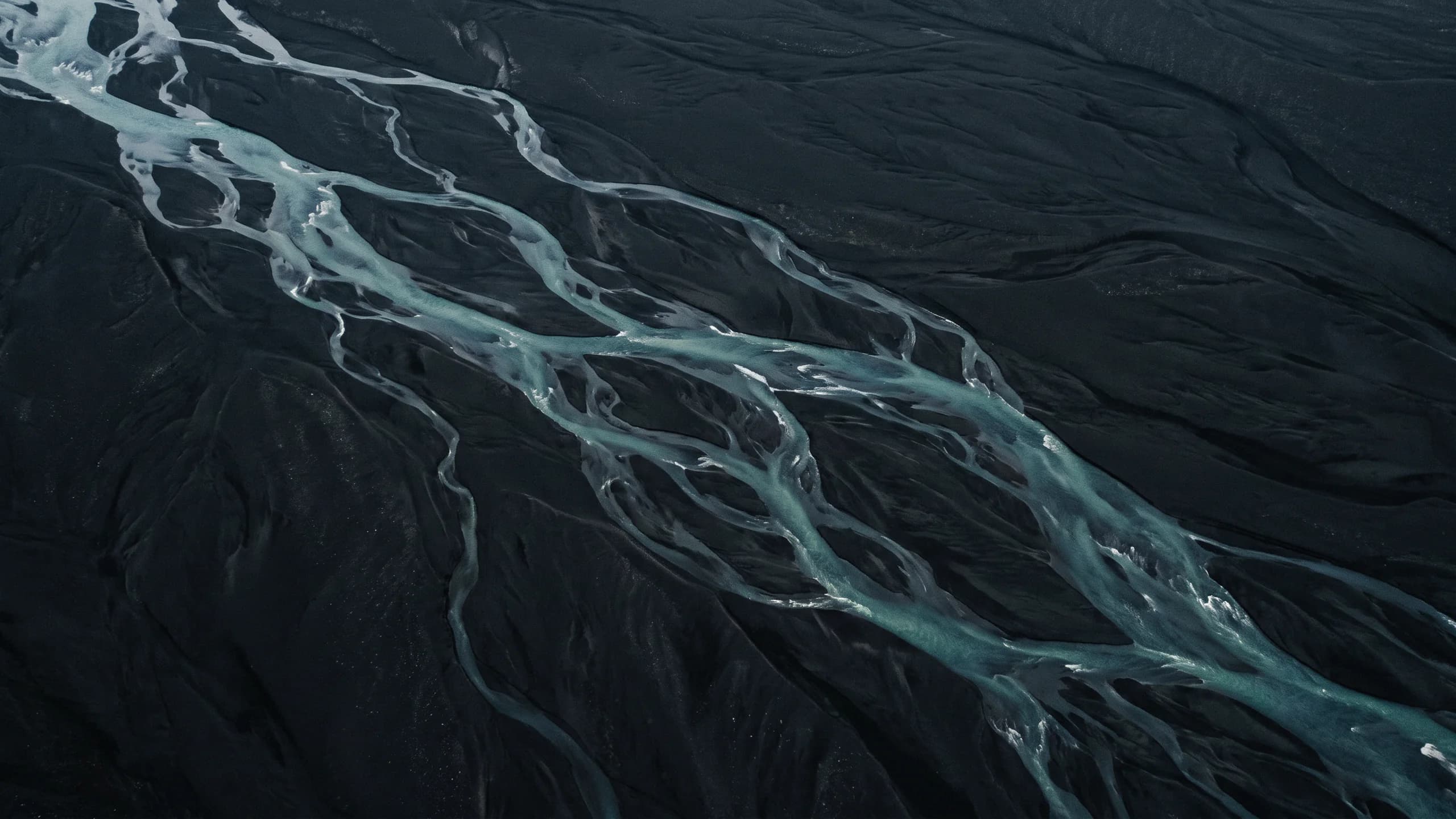 Aerial view of a braided glacial river crossing black sand.